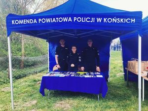 Zdjęcie przedstawiające namiot wystawienniczy koloru niebieskiego z napisem Komenda Powiatowa Policji w Końskich, pod którym stoi trójka umundurowanych policjantów.