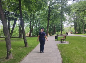 Zdjęcie umundurowanej policjantki idącej aleją parkową