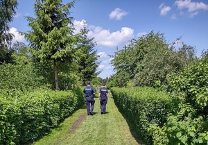 Zdjęcie dwójki umundurowanych policjantów idących alejką ogrodową.