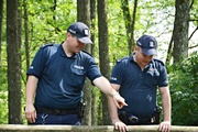 Zdjęcie dwóch umundurowanych policjantów na leśnej polanie.