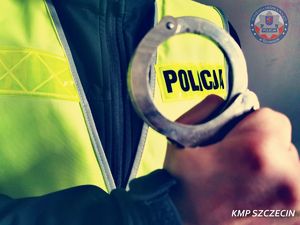 zdjęcie zapiętych kajdanek trzymanych w ręce przez umundurowanego policjanta.