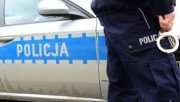 Zdjęcie boku radiowozu i nogi umundurowanego policjanta.