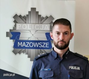 Umundurowany policjant z zarostem na twarzy, w tle gwiazda policyjna.