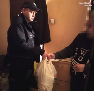 Umundurowany policjant podający torbę starszemu mężczyźnie wewnątrz mieszkania.