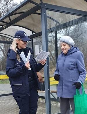 Wiata komunikacji miejskiej pod którą stoją młoda, umundurowana policjantka i kobieta w starszym wieku.