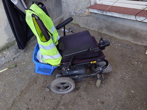 Elektryczny wózek inwalidzki z założoną na oparciu żółtą kamizelką.