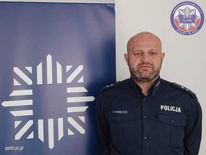 Umundurowany policjant na tle loga Policji.