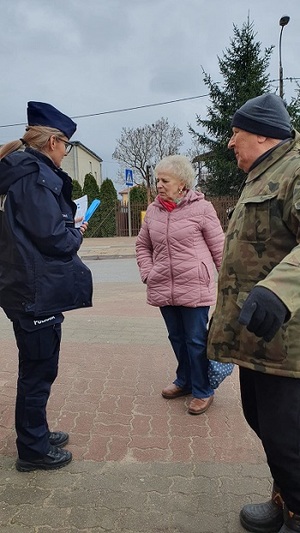 Umundurowana policjantka rozmawiająca z dwójką starszych osób na tle ulicy.