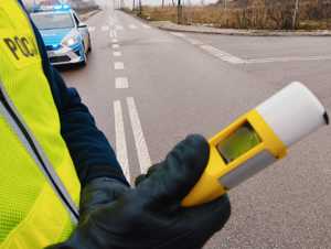 Zbliżenie urządzenia alko sensor w kolorze żółtym trzymanego w dłoniach policjanta,  w tle ulica.