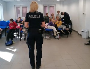 Sala lekcyjna z grupką dzieci oraz dwójką umundurowanych policjantów.