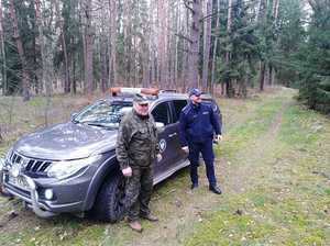Samochód terenowy w scenerii leśnej, przed którym stoi policjant i funkcjonariusz Państwowej Straży Łowieckiej.