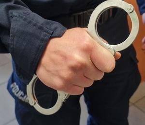 Zbliżenie dłoni umundurowanego policjanta trzymającego w niej kajdanki.