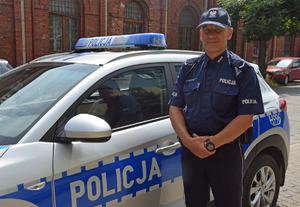 Policjant przy radiowozie, na tle budynku z czerwonej cegły