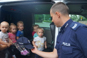 Grupa dzieci siedząca w radiowozie typu bus, na pierwszym planie obrócony bokiem umundurowany policjant