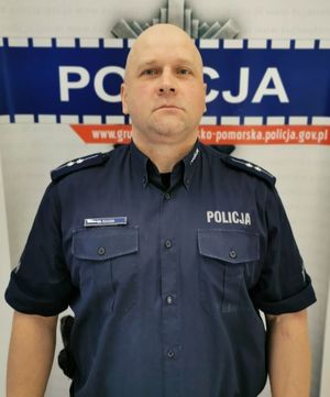 Umundurowany policjant na tle loga kujawsko-pomorskiej Policji
