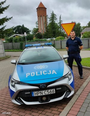 Umundurowany policjant stojący na ulicy obok radiowozu