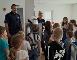 Sala z dziećmi tłoczącymi się przy dwójce umundurowanych policjantów