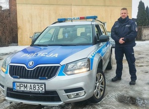 Umundurowany policjant obok radiowozu na tle budynku