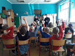 Sala szkolna wypełniona dziećmi oraz dwaj umundurowani policjanci