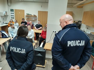 zdjęcie sali z siedzącymi młodymi osobami niepełnosprawnymi oraz dwójka policjantów prowadząca prelekcję