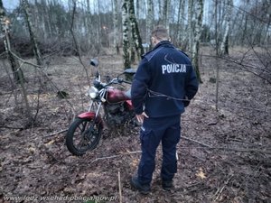 Motocykl w brzozowym lesie, a przy nim stojący policjant