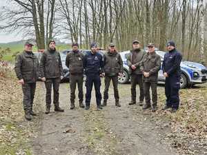 Grupa leśników i policjantów na tle radiowozów w lesie
