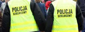 Zbliżenie widzianych od tyłu dwóch policjantów w kamizelkach odblaskowych z napisem Policja Dzielnicowy