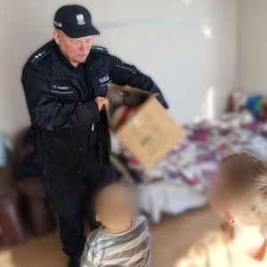 Umundurowany policjant z kartonowym pudłem wśród dzieci - zdjęcie zanonimizowane