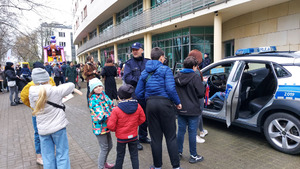 Grupa dzieci przy radiowozie stojącym na ulicy, obok umundurowany policjant