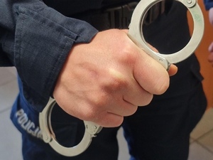 Zbliżenie dłoni policjanta trzymającej srebrne kajdanki