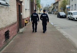 Dwóch policjantów idących chodnikiem wzdłuż kamienicy