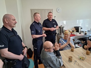 Trzech munudurowanych policjantów w pomieszczeniu z grupą siedzących przy stole  seniorów