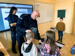 Dwoje umundurowanych policjantów z dziećmi  w pomieszczeniu przedszkola