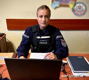 W pomieszczeniu za biurkiem siedząca na krześle umundurowana policjantka