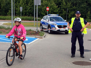 Dziecko jadące na rowerze w tle umundurowany policjant i oznakowany radiowóz