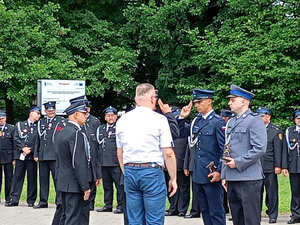 Policjanci i strażacy w umundurowaniu wyjściowym na tle zieleni