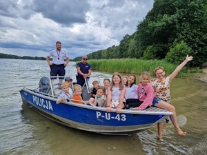 Dwóch umundurowanych policjantów z grupą dzieci, przy brzegu  na policyjnej łodzi