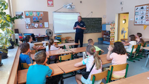 Policjant w sali szkolnej wypełnionej dziećmi w ławkach