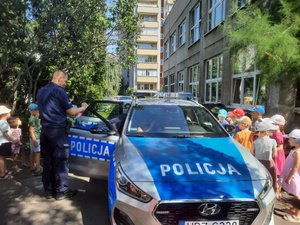 Radiowóz na osiedlu, na zewnątrz policjant i grupa przedszkolaków