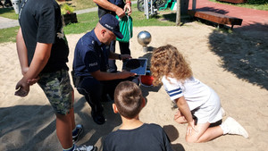 Grupa dzieci i ich opiekunów oraz policjant w piaskownicy