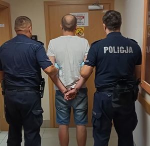 Dwóch policjantów prowadzi meżczyznę zakutego w kajdanki