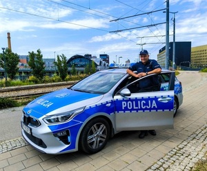 Umundurowany policjant stoi przy oznakowanym radiowozie