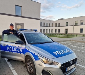 Umundurowany Policjant z oznakowanym radiowozem