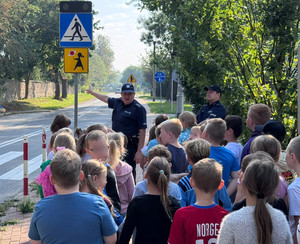 Dwaj policjanci w rejonie skrzyżowania prowadzący pogadankę dla grupki dzieci