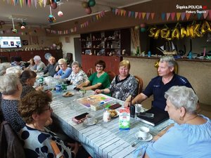 grupa seniorów siedząca w świetlicy przy stole wraz z policjantem