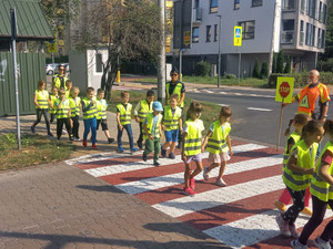 Grupka dzieci ubranych w odblaskowe kamizelki przechodząca przez przejście dla pieszych