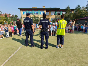 Grupka dzieci na boisku szkolnym, Na pierwszym planie widać dwóch policjantów