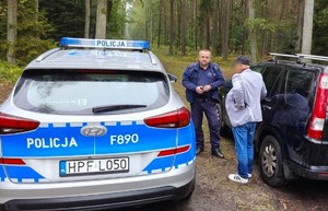 Zdjęcie przedstawiające policjanta wraz z radiowozem w trakcie interwencji wobec mężczyzny na drodze leśnej.