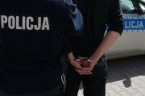 Policjant prowadzi mężczyznę w kajdankach zapiętych z tyłu