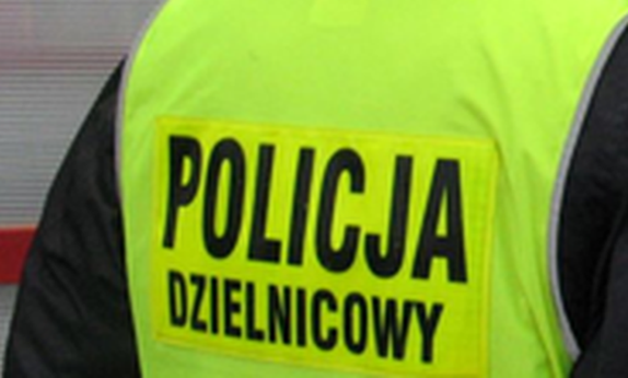 Zbliżenie pleców policjanta w żółtej kamizelce odblaskowej z napisem Policja Dzielnicowy